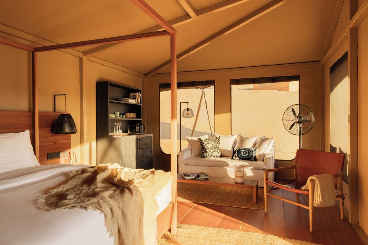 Ein Schlafzimmer mit einem Himmelbett, einem Schlafsofa, einem Sessel und einem Ventilator.