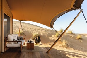 A desert tent with a sofa and coffee table, surrounded by sand dunes. - Amar Luxury Desert Ecolodge (Al 'Ajban)