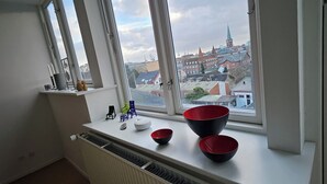 A room with a window overlooking a cityscape, a radiator below the window, and a shelf with small chairs and bowls. - Central apartment with panoramic view and roof terrace   (Aarhus)