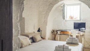 A bedroom with a bed, pillows, a lamp, a TV, and towels.
