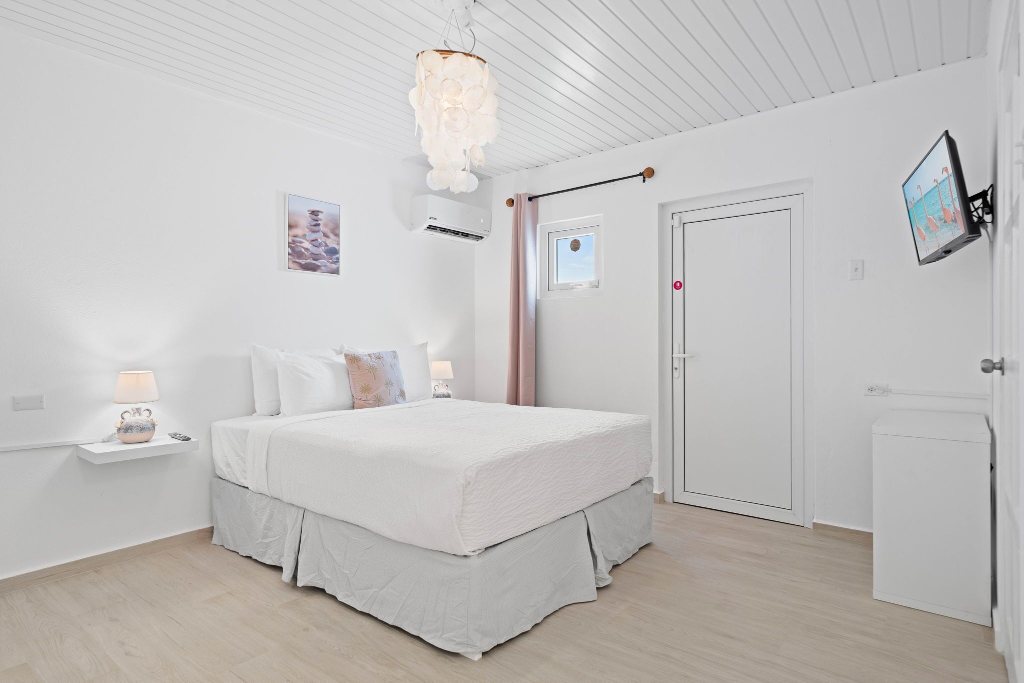 A bedroom with a bed, bedside table, lamp, air conditioning unit, and a television on the wall.