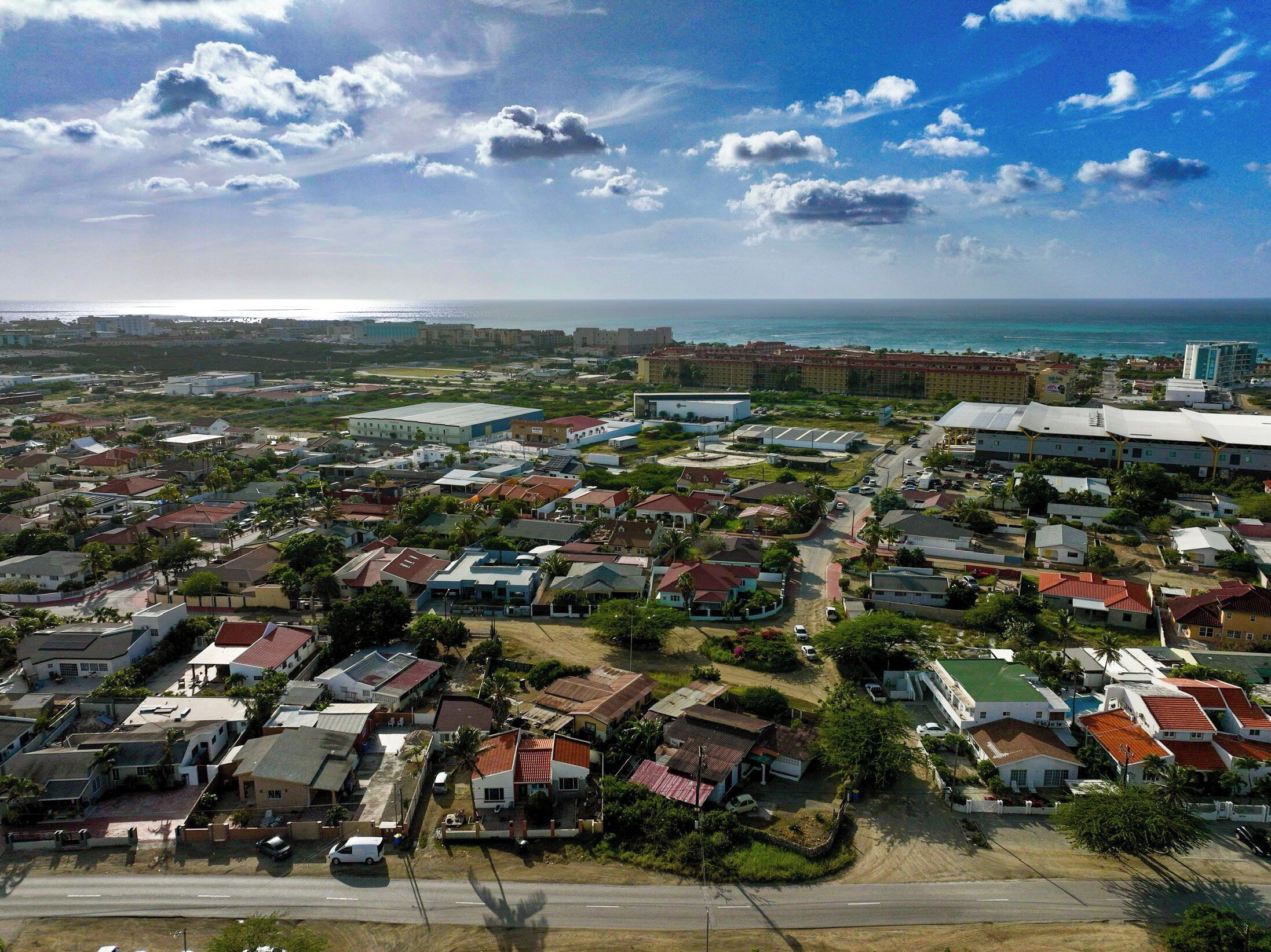 An aerial view of a coastal residential area with houses, roads, and a large building complex.