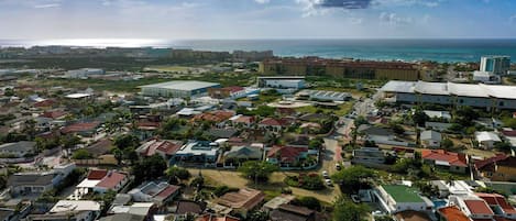 An aerial view of a coastal residential area with houses, roads, and a large building complex.