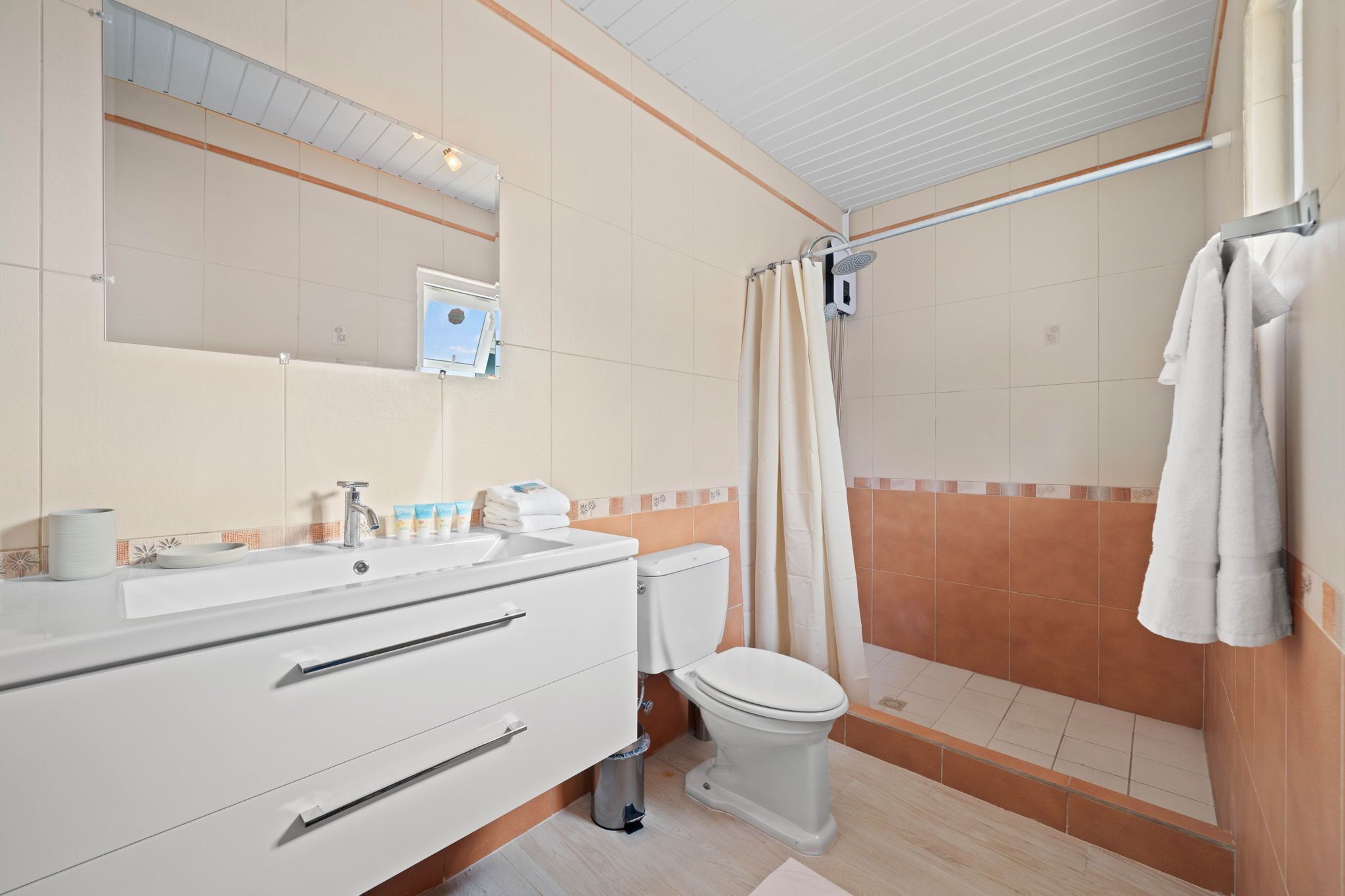 Ein Badezimmer mit weißem Waschbecken, Spiegel und Toilette, einer Duschkabine mit Vorhang und einem Handtuchhalter.