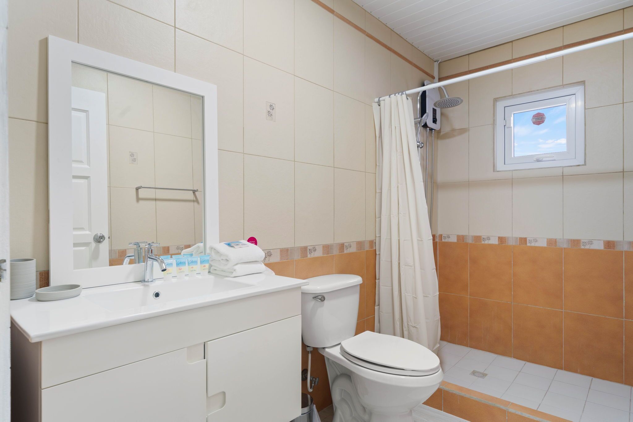 Un baño con lavamanos blanco, espejo, inodoro y cortina de ducha.