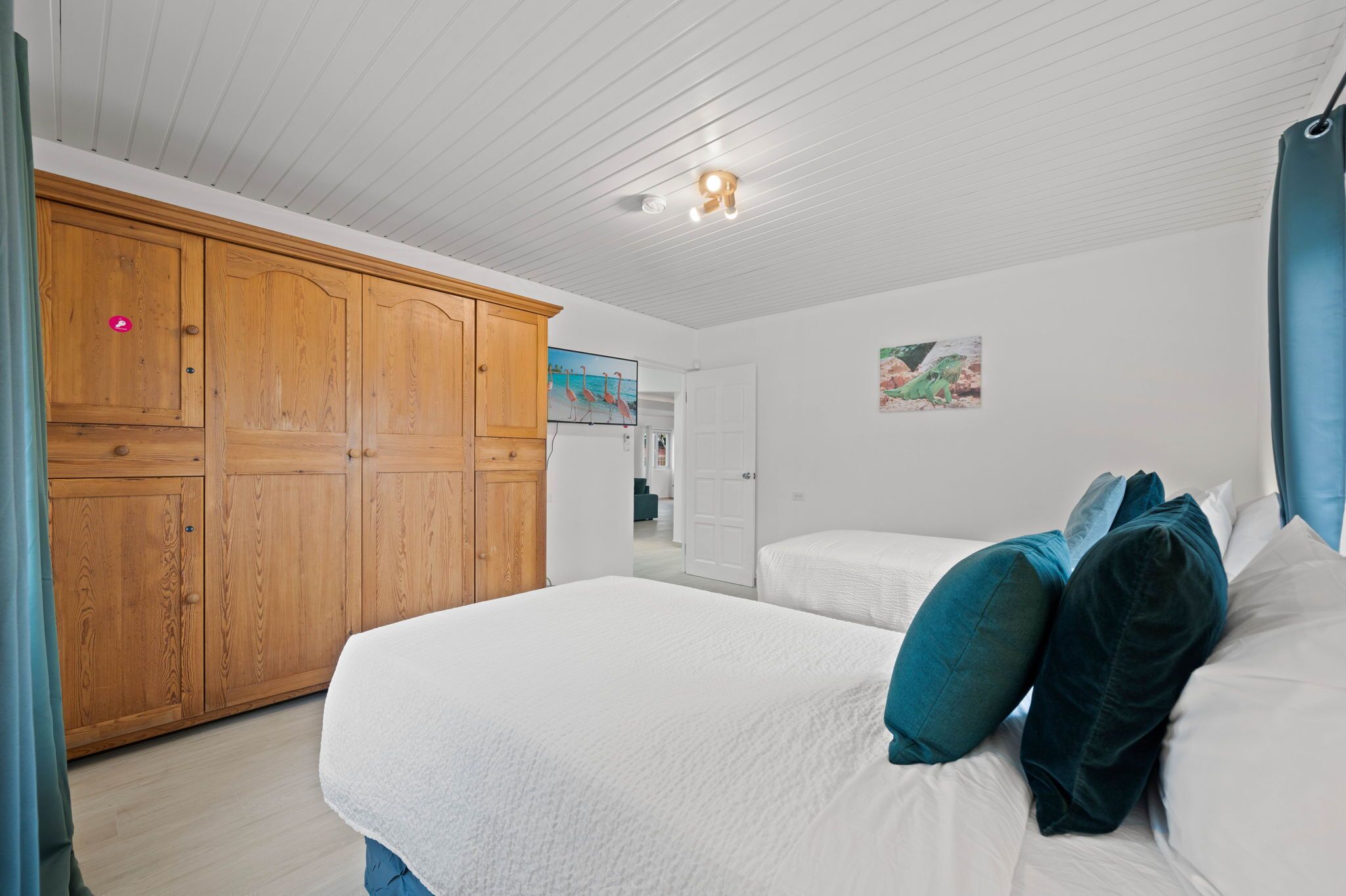 Ein Schlafzimmer mit großem Holzschrank, einem Bett mit weißer Bettwäsche und türkisfarbenen Kissen sowie einer Deckenleuchte.