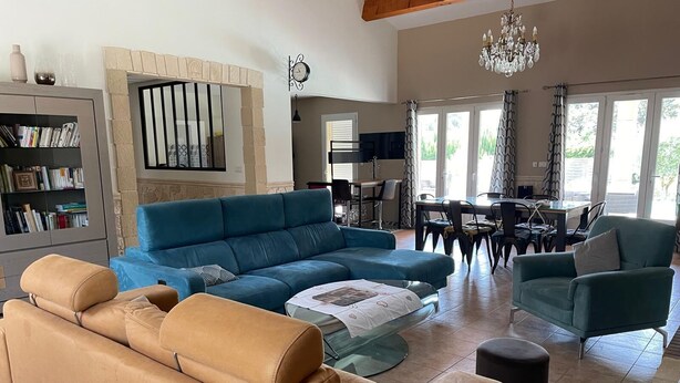 A spacious living room with a large blue sofa, a tan leather sofa, and a dining area with a table and chairs.