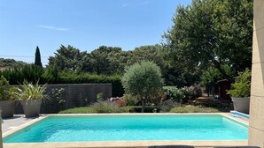 A rectangular swimming pool with a tiled deck, surrounded by potted plants and trees.