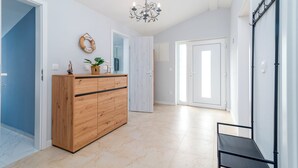 A spacious hallway with a wooden cabinet, a chandelier, and a door leading to another room. - Stunning apartment with breathtaking sea view (Mastrinka)