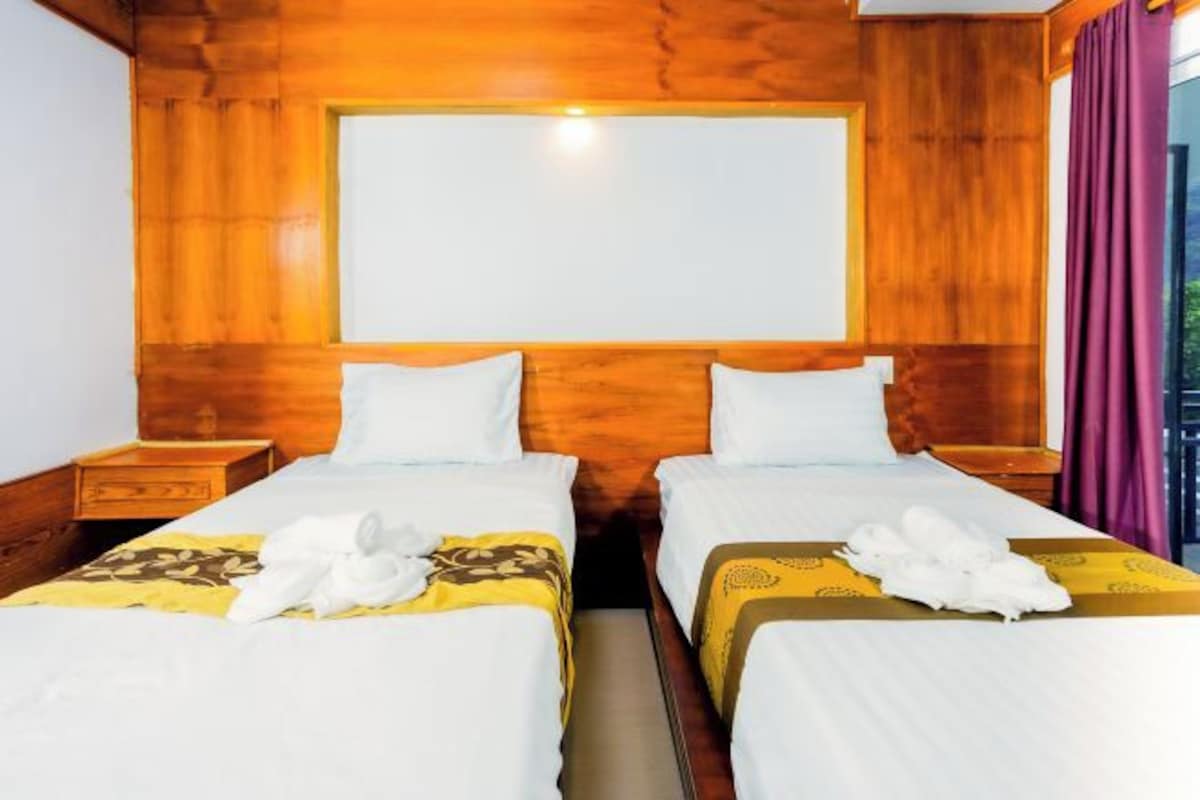 A hotel room with two beds, wooden paneling, and a large window.