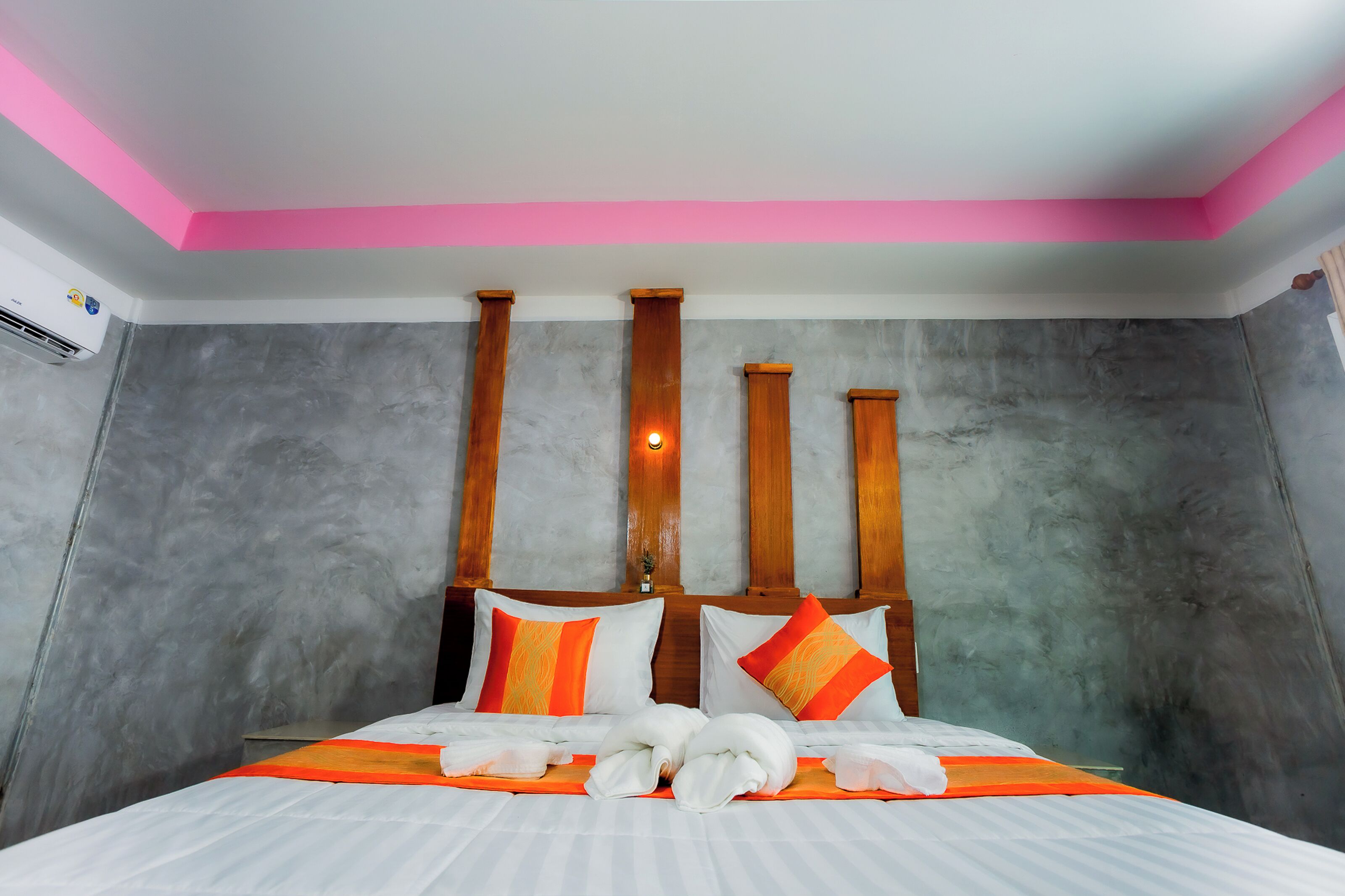 A hotel room with a bed, a headboard with vertical wooden slats, and a pink ceiling.