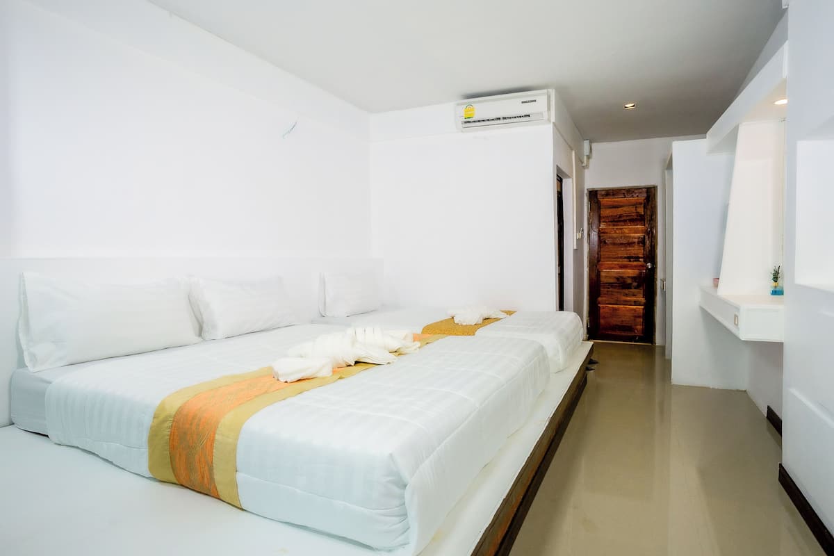 A hotel room with two beds, a wooden door, and a white wall with an air conditioning unit.