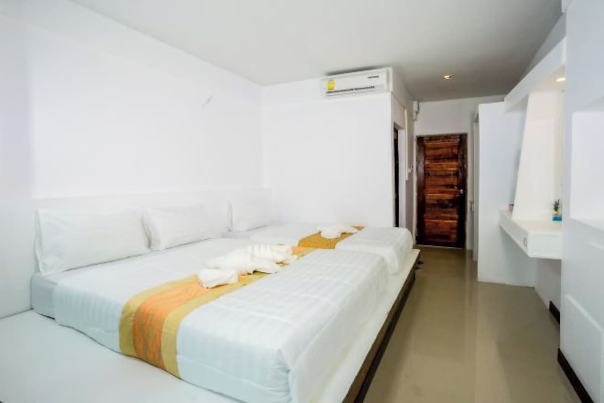 A hotel room with a bed, a bedside table, an air conditioning unit, and a wooden door.