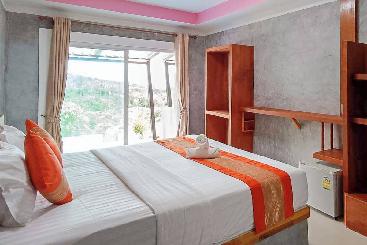 A hotel room with a bed, a desk, a small refrigerator, and a window with a view of the outdoors.