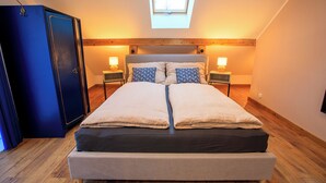 A bedroom with a bed, two bedside tables with lamps, a wardrobe, and a skylight.