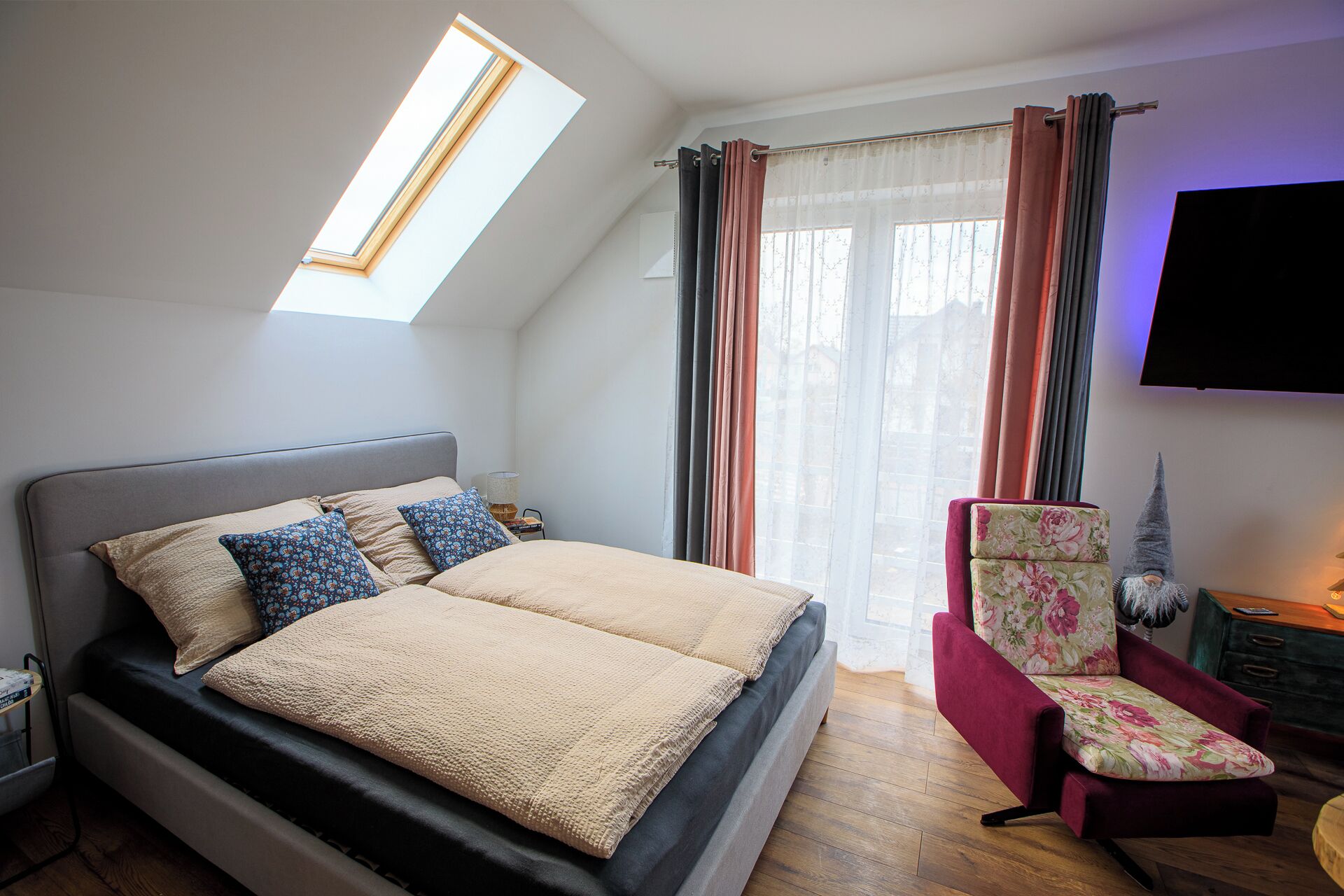 A bedroom with a bed, a chair, a gnome decoration, and a TV.
