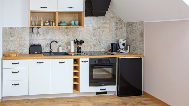 A compact kitchen with white cabinets, a wooden countertop, a built-in oven, and a coffee maker.