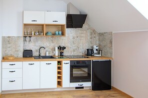 Uma cozinha compacta com armários brancos, bancada de madeira, forno embutido e cafeteira.