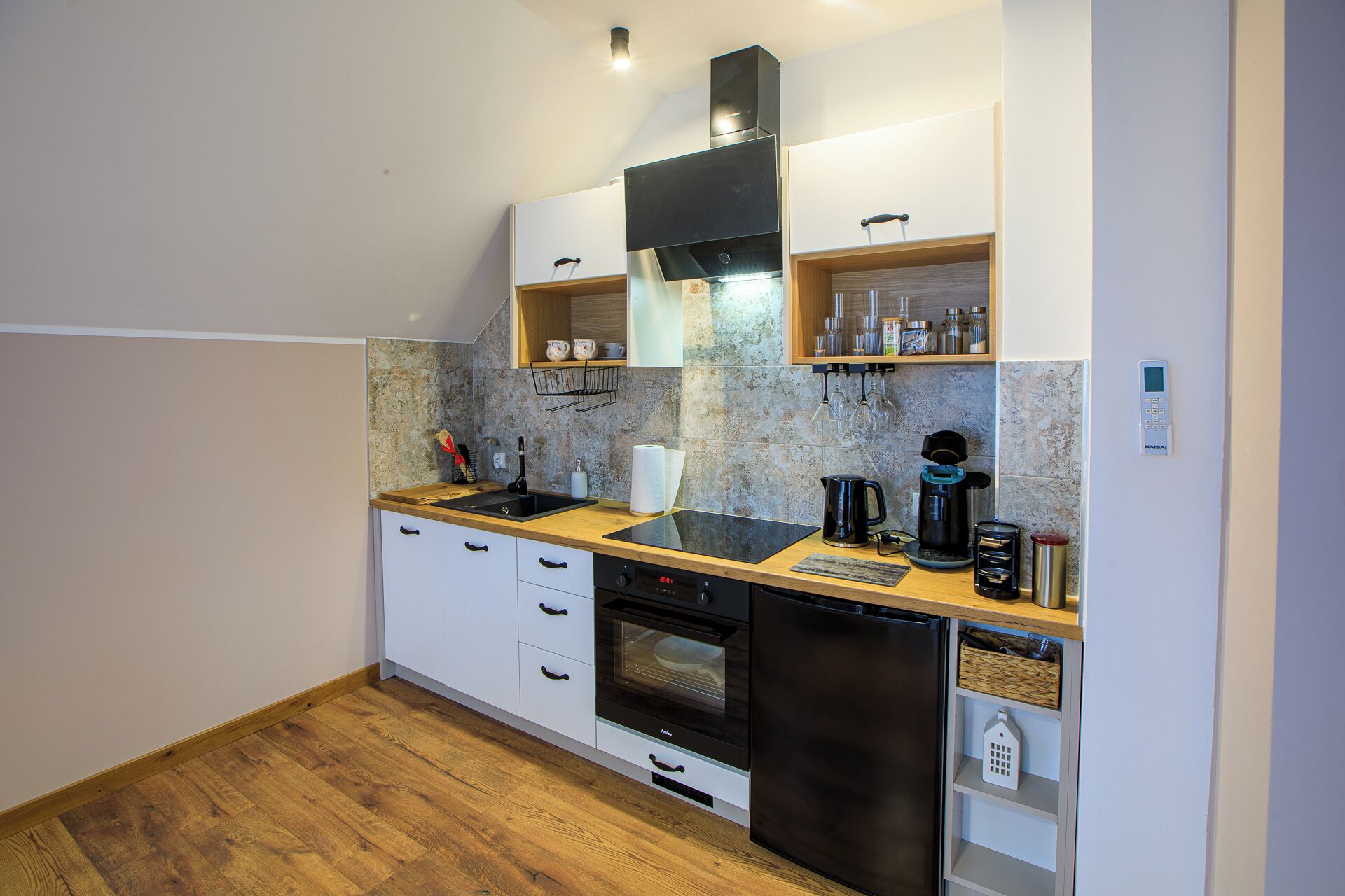 A compact kitchen with white cabinets, a black range hood, a built-in oven, and a coffee machine.