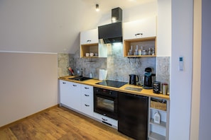 A compact kitchen with white cabinets, a black range hood, a built-in oven, and a coffee machine.