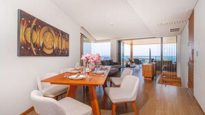 A modern dining area with a wooden table set for four, white cushioned chairs, and a large abstract painting on the wall. - Luxury 2BR Apartment in Bluepoint 82 (Patong)