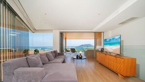 A modern living room with a large sectional sofa, a wooden entertainment unit, and a television. - Luxury 2BR Apartment in Bluepoint 82 (Patong)
