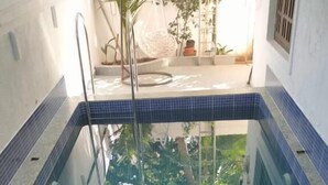 En swimmingpool med blå kakelplattor, omgiven av en vit vägg och ett metallräcke.