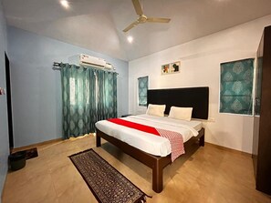 Ein Schlafzimmer mit einem Bett, einem Deckenventilator, einer Klimaanlage, einem Fenster mit Vorhängen und einem gemusterten Teppich.