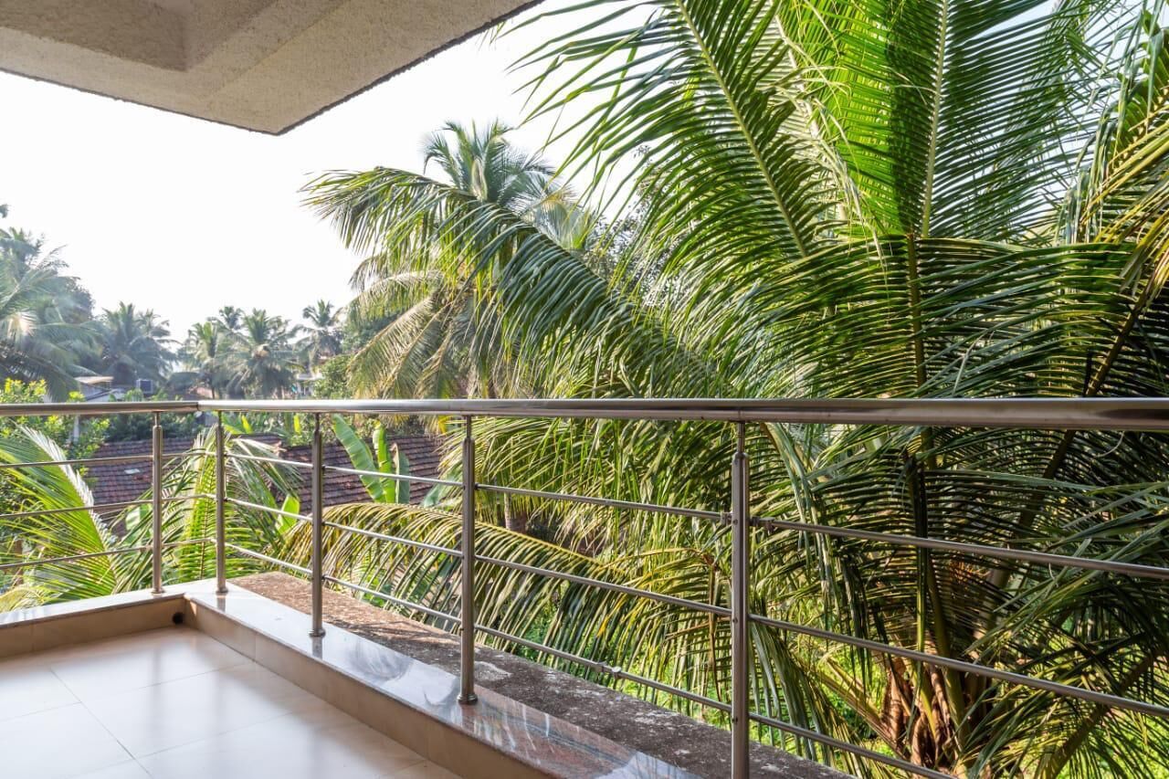 A balcony with a metal railing overlooking a lush garden with palm trees.