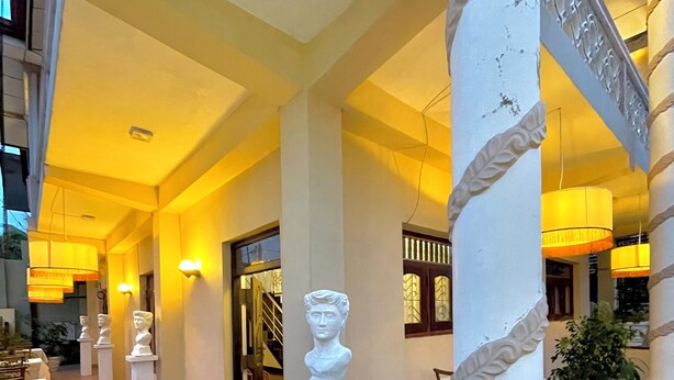 A corridor with white columns, a staircase, and a dining area with tables and chairs. - Rivinson (Negombo)