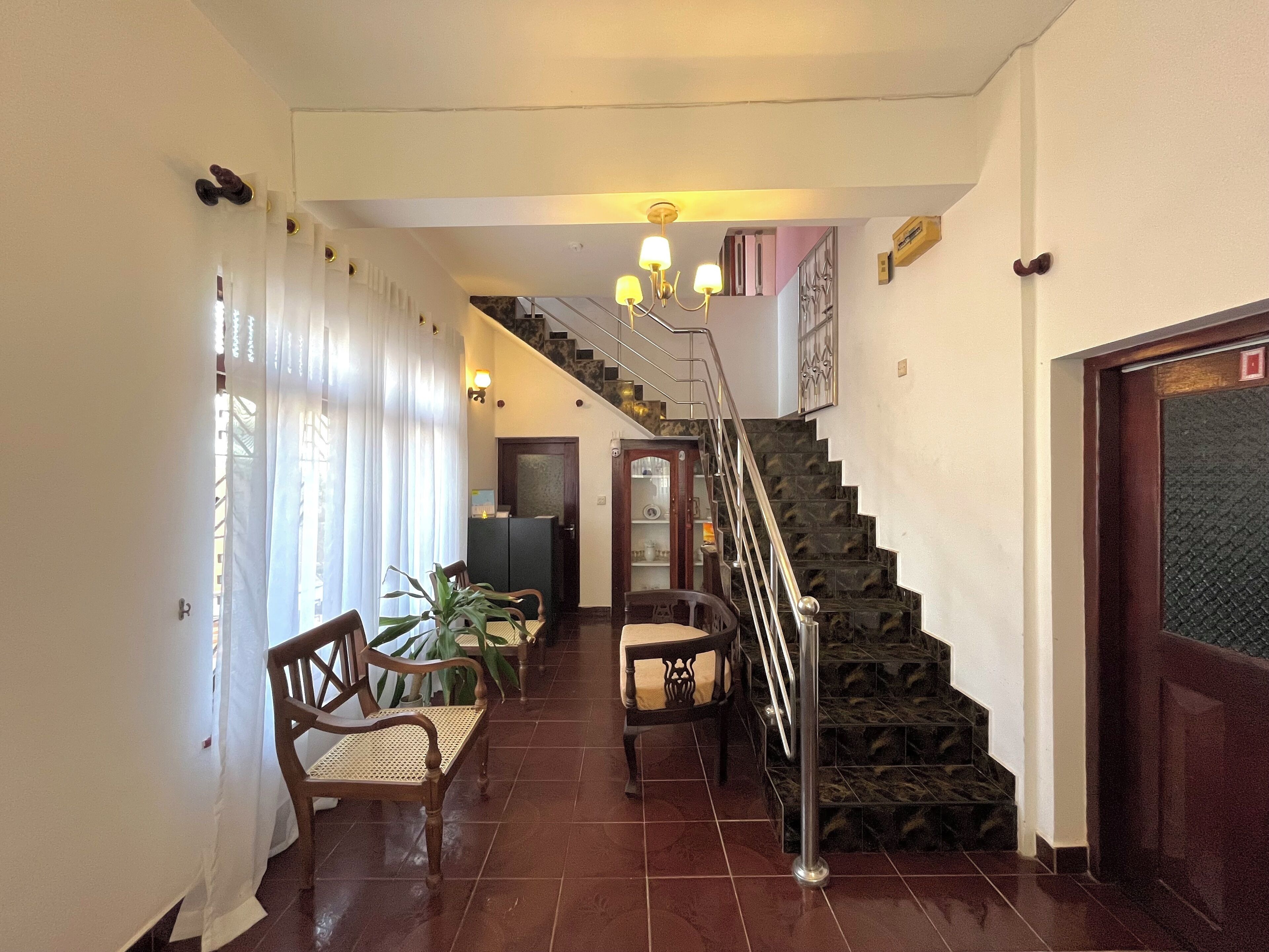 A hallway with a staircase, wooden chairs, a table, and a potted plant.