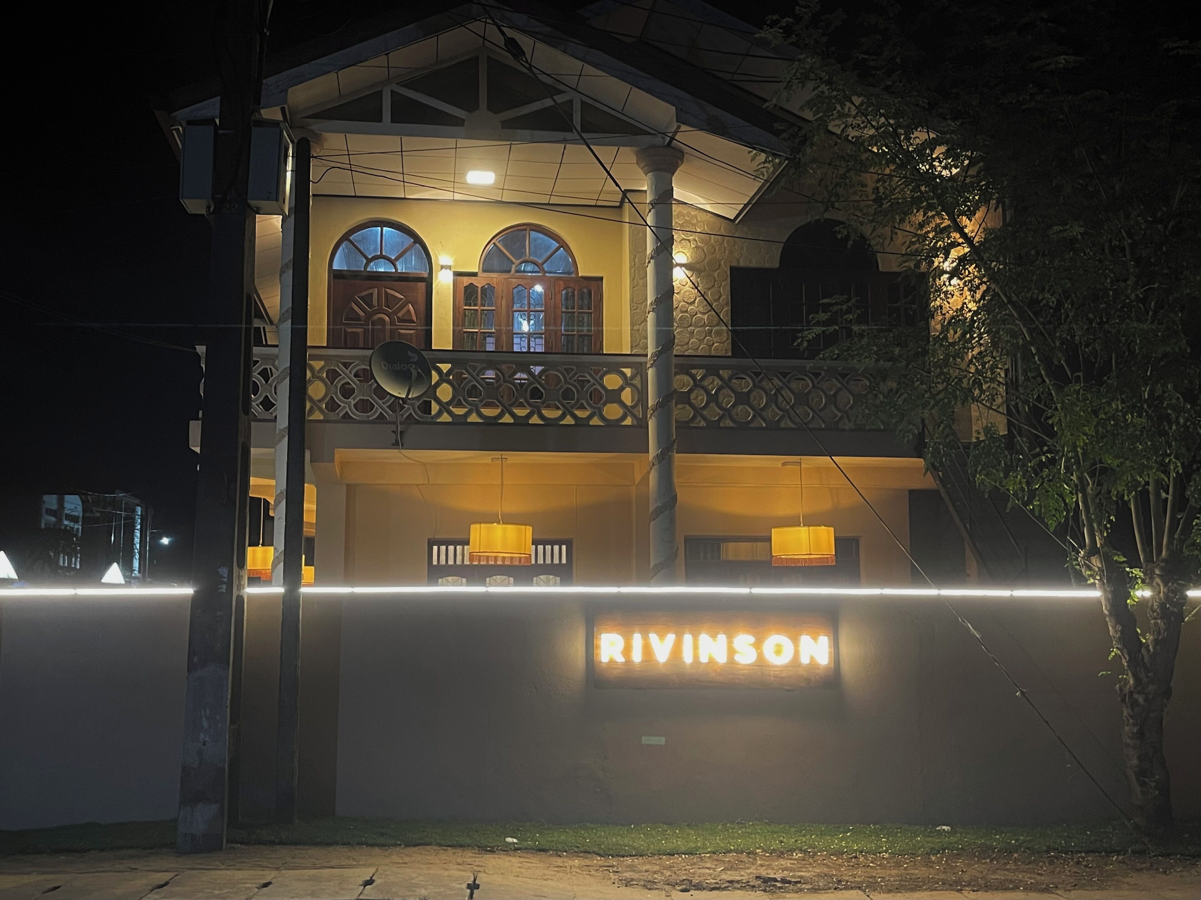 Un edificio con un letrero que dice "RIVINSON" en la entrada, que cuenta con un balcón con barandilla y un gran ventanal encima.