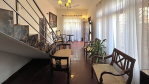 A staircase with metal railings, a chandelier, and a dining area with wooden chairs and a table. - Rivinson (Negombo)