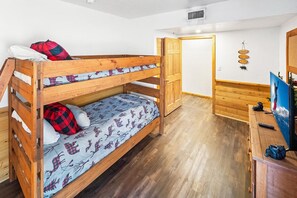 A bunk bed room with a wooden floor, a desk with a computer, and a door leading to another room.
