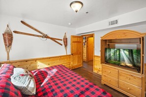 A room with a bed, a wooden dresser, a television, and a door leading to another room.
