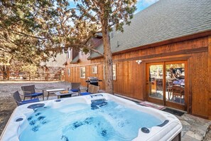 A hot tub in a backyard with a wooden fence, outdoor furniture, and a tree.