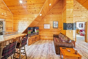 A log cabin interior with a bar area, seating, and a dartboard.