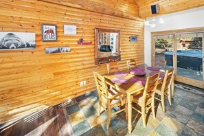 Interior de uma cabana de madeira com uma mesa de jantar, cadeiras, um espelho e decorações com tema de ursos.