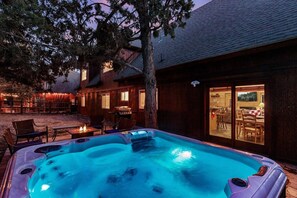 Un jacuzzi en un patio trasero con una casa de madera y mobiliario exterior.