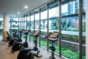 A gym with multiple stationary bikes and a large window overlooking a landscaped area. - 2BR R&F Phase2, CIQ R&F Mall, Free Parking (Johor Bahru)