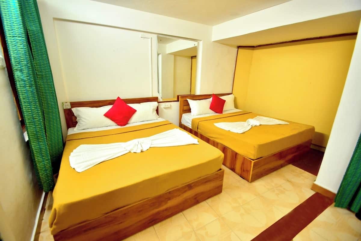 A hotel room with two beds, each with a wooden headboard, white bedding, and red pillows. There is a mirror on the wall and a green curtain partially visible.