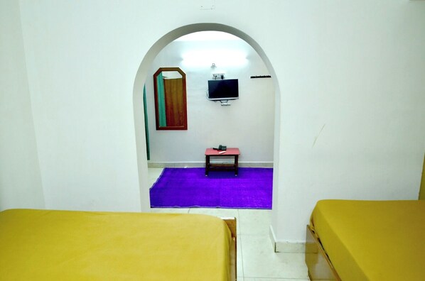 A room with two yellow beds, a purple carpet, a small table with a red stool, a TV on the wall, and a mirror. - Estay SK Residency (Ootacamund)