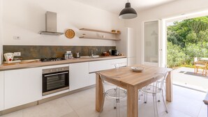 A modern kitchen with a wooden table, clear chairs, a built-in oven, and a large window. - Villa Plemmiria by the Sea by Wonderful Italy (Syracuse)