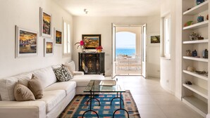 A living room with a sofa, a glass coffee table, a patterned rug, and a view of the sea through an open door. - Villa Plemmiria by the Sea by Wonderful Italy (Syracuse)