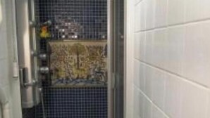 Zona de dutxa petita i tancada, amb paret de rajola i porta metàl·lica.