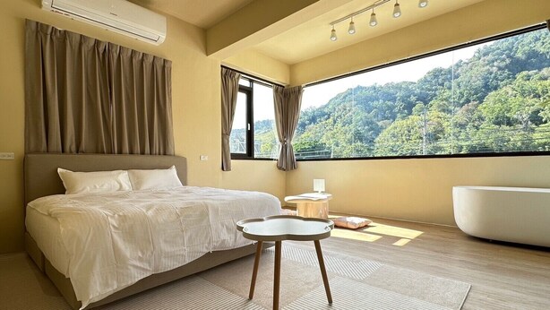 A bedroom with a bed, a round table, a bathtub, and a large window with a forest view. - Here after us (Dahu)