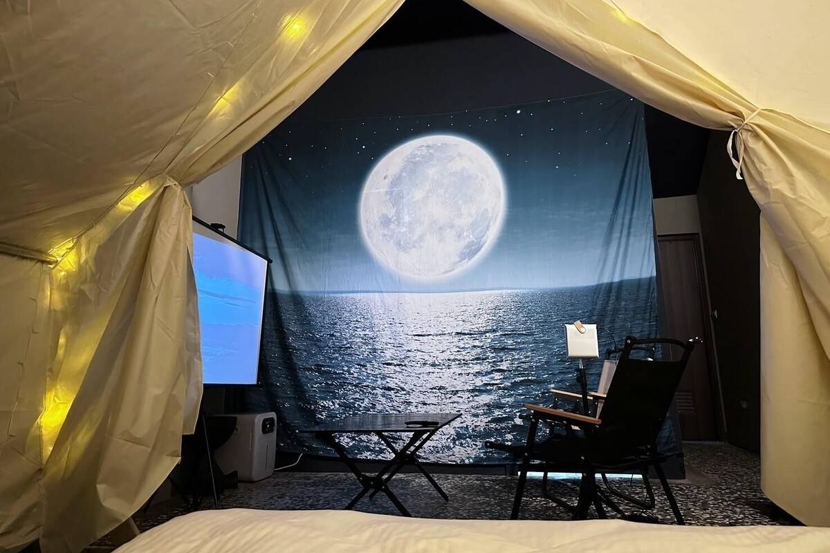 A cozy tented room with a large moon and stars backdrop, a comfortable chair, and a television.