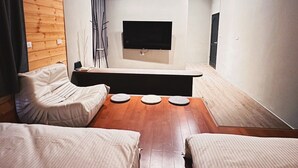 A modern living room with a flat-screen TV mounted on the wall, a wooden floor, and a seating area with a sofa and two armchairs. - Here after us (Dahu)