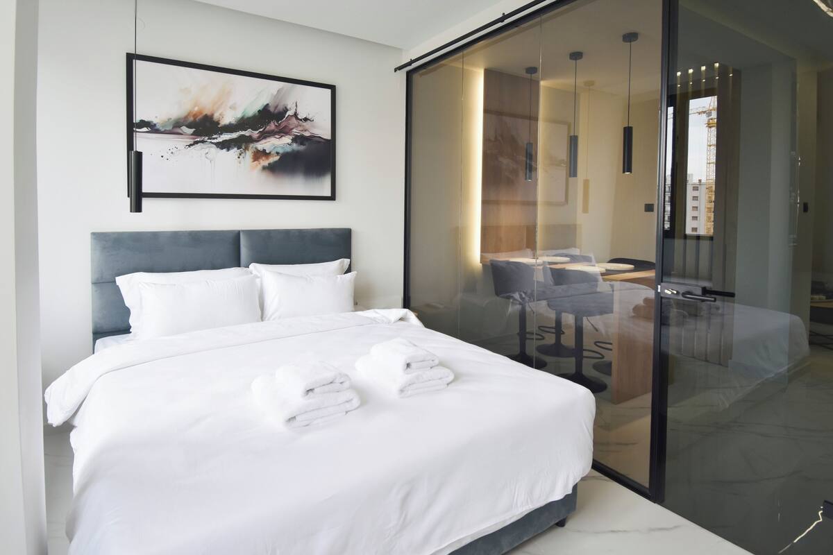 Ein modernes Hotelzimmer mit einem großen Bett, einer Glastrennwand, einem Schreibtisch und einem Sessel.