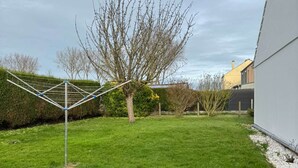 A grassy yard with a clothesline, a tree, and a building in the background. - Le Rivage, House with garden near the sea (Saint-Aubin-sur-Mer)